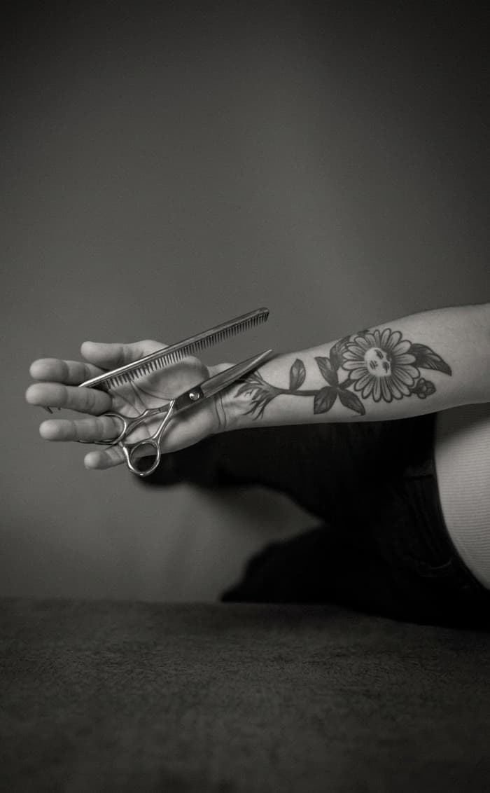 Tattooed hand holding scissors and a comb